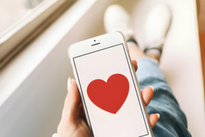 Une main tenant un smartphone affichant un grand cœur rouge sur l'écran.