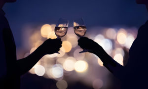 Silhouettes d'un couple portant un toast avec des verres de vin devant un fond flou de lumières de la ville.