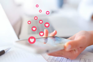 Une personne utilisant son smartphone avec des icônes de cœur flottant au-dessus de l'écran, symbolisant probablement l'interaction avec des applications de rencontres.