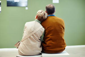 Un couple âgé assis côte à côte dans une salle d'attente, se tenant par l'épaule.