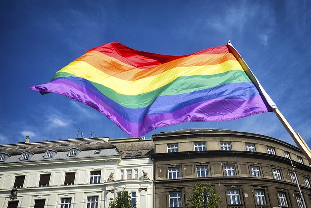 Drapeau arc-en-ciel de la fierté LGBTQ+ flottant fièrement devant un bâtiment en journée ensoleillée.