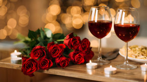 Un bouquet de roses rouges avec deux verres de vin sur une table éclairée par des bougies.