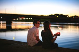 Couple assis au bord de l'eau tenant un cierge magique la nuit.