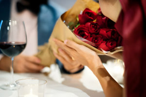 Une personne tenant un bouquet de roses rouges lors d'un dîner romantique.